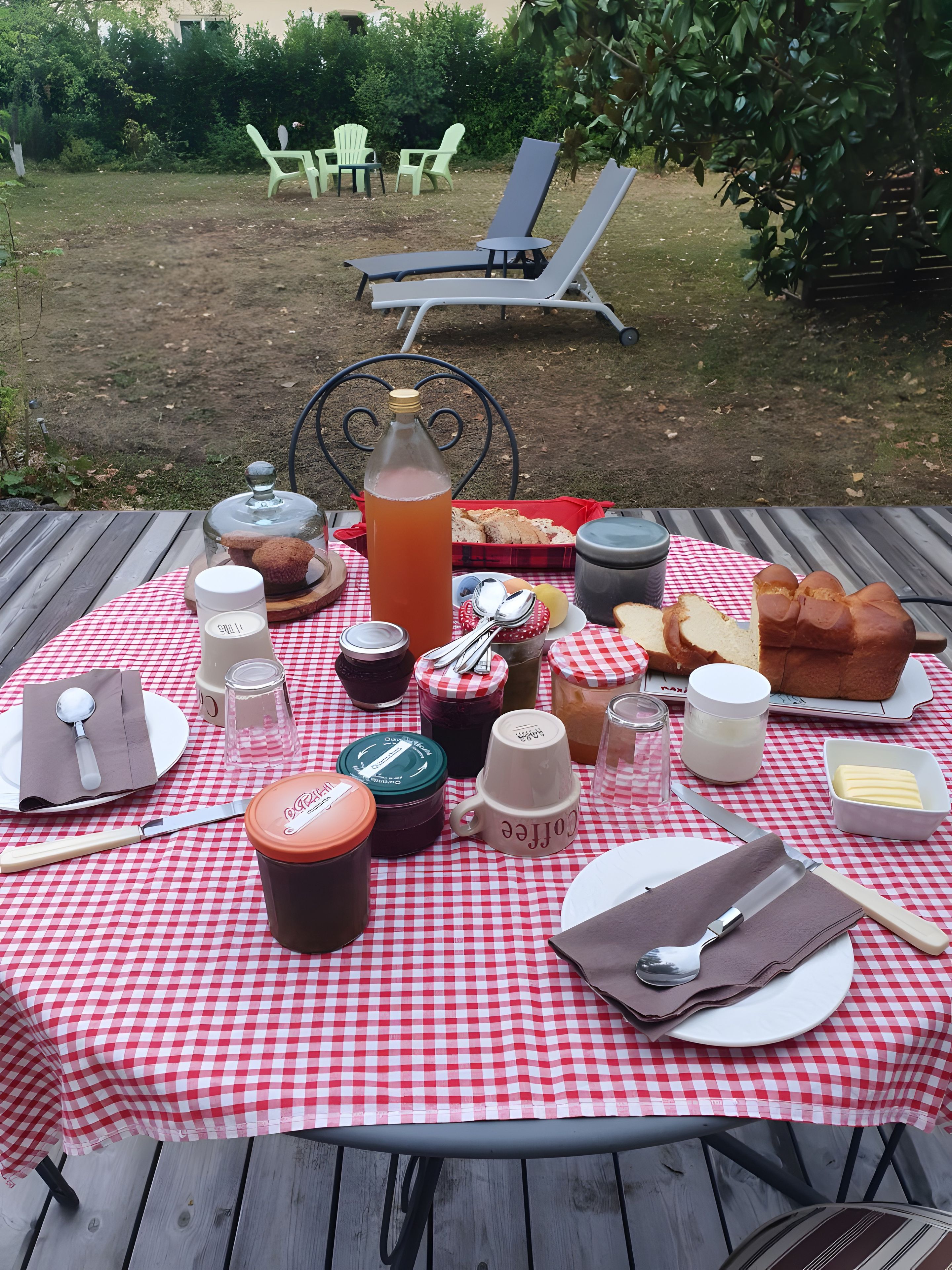 En picknickuppsättning med ett rutigt bordstäcke, olika sorters mat, tillbehör och en flaska iste.