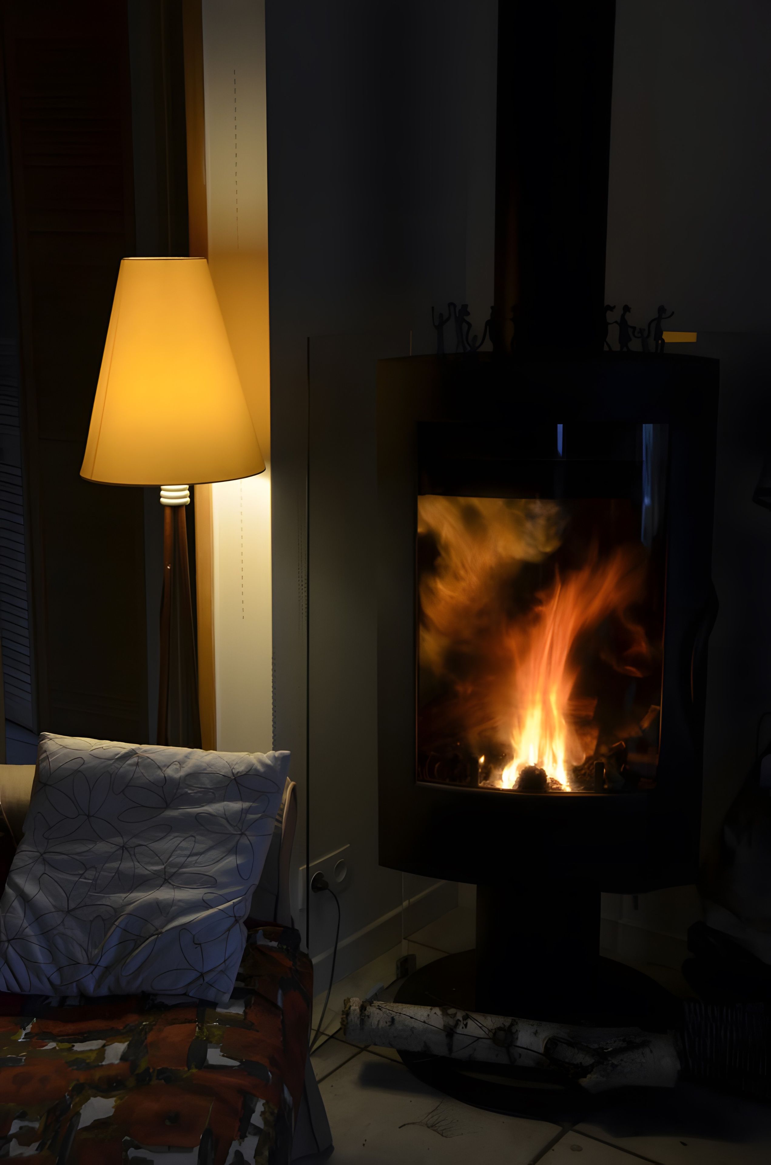 Ett rum med en vedeldad kamin, en lampa och en mönstrad kudde.