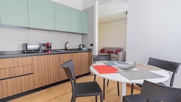 A modern kitchen with a built-in oven, a coffee machine, and a kettle. There is a dining area with a round table and four chairs.