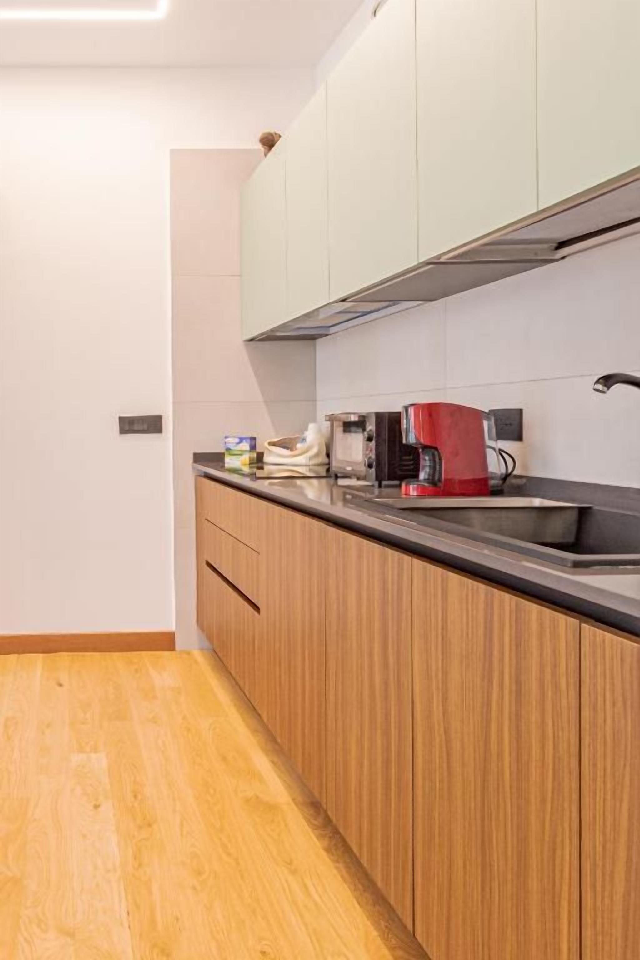 Una cocina moderna con armarios de madera, encimera negra y una cafetera roja.