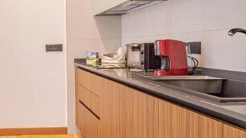 Una cocina moderna con armarios de madera, encimera negra y una cafetera roja.