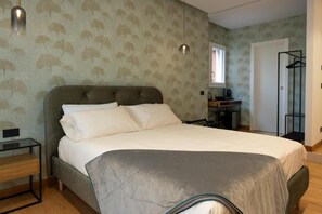 A bedroom with a large bed, a bedside table, a wardrobe, and a window. - Colour Suite (NAPOLI)