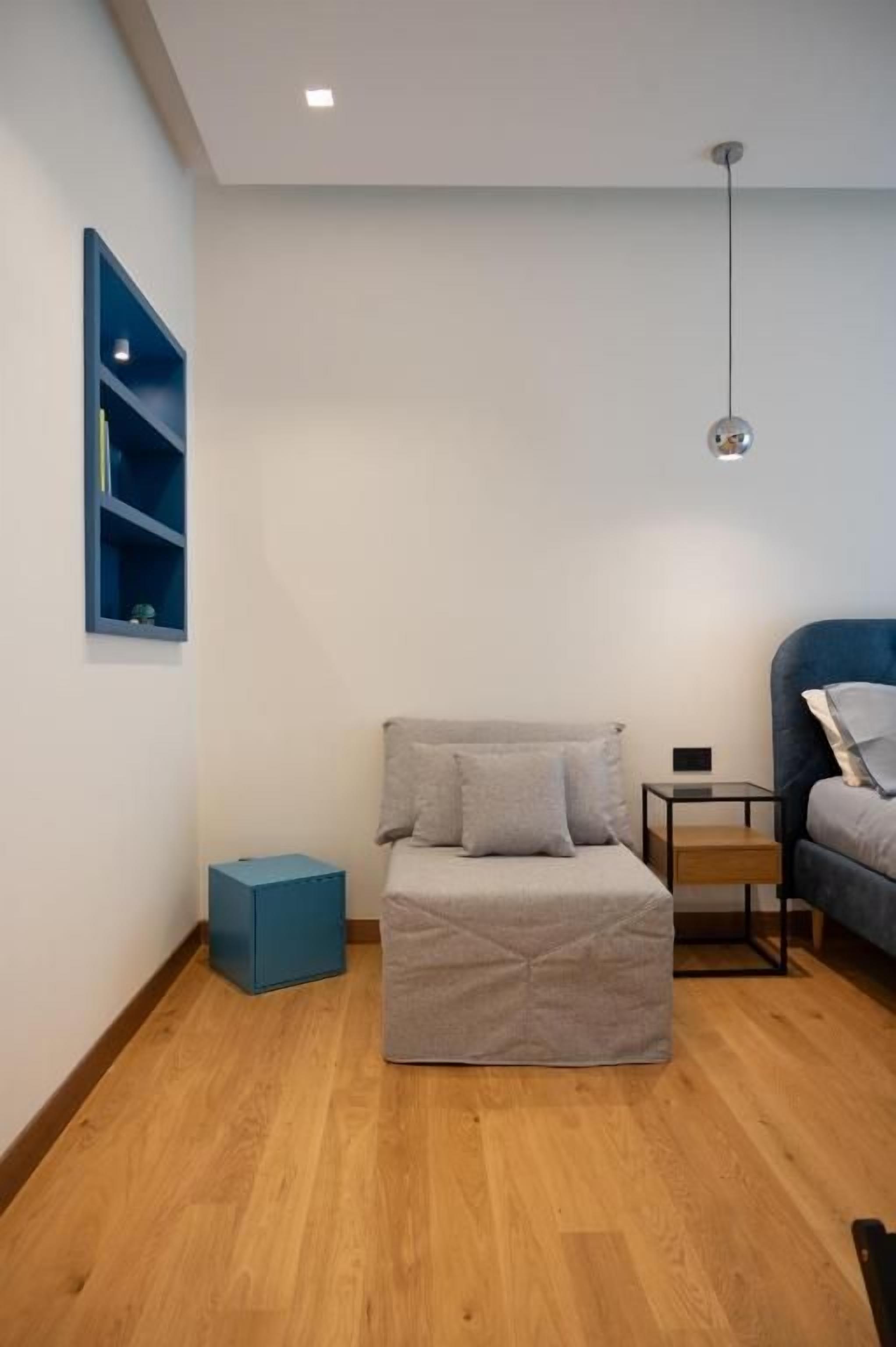 A room with a bed, a small table, a blue storage unit, and a hanging light fixture.