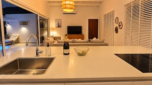 A modern kitchen with a built-in sink, a bottle of champagne, and a fruit bowl on the counter. - Cas Seida - Private Pool Villa Pure Aruba (Oranjestad)