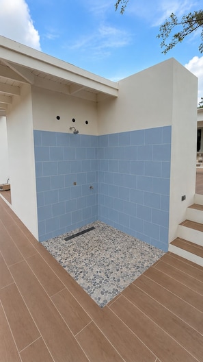 A modern outdoor shower area with blue tiles and a pebble-patterned floor. - Cas Seida - Private Pool Villa Pure Aruba (Oranjestad)