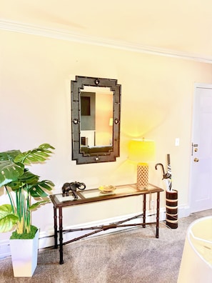 A room with a mirror, a console table, a potted plant, a lamp, and an umbrella.