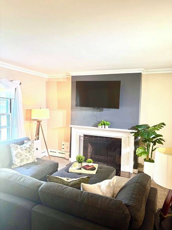 A living room with a sofa, a flat-screen TV mounted above a fireplace, and a lamp.