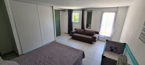 A room with a bed, a sofa, a window with curtains, and a pet bed. - Vrbo Property (Porto-Vecchio)
