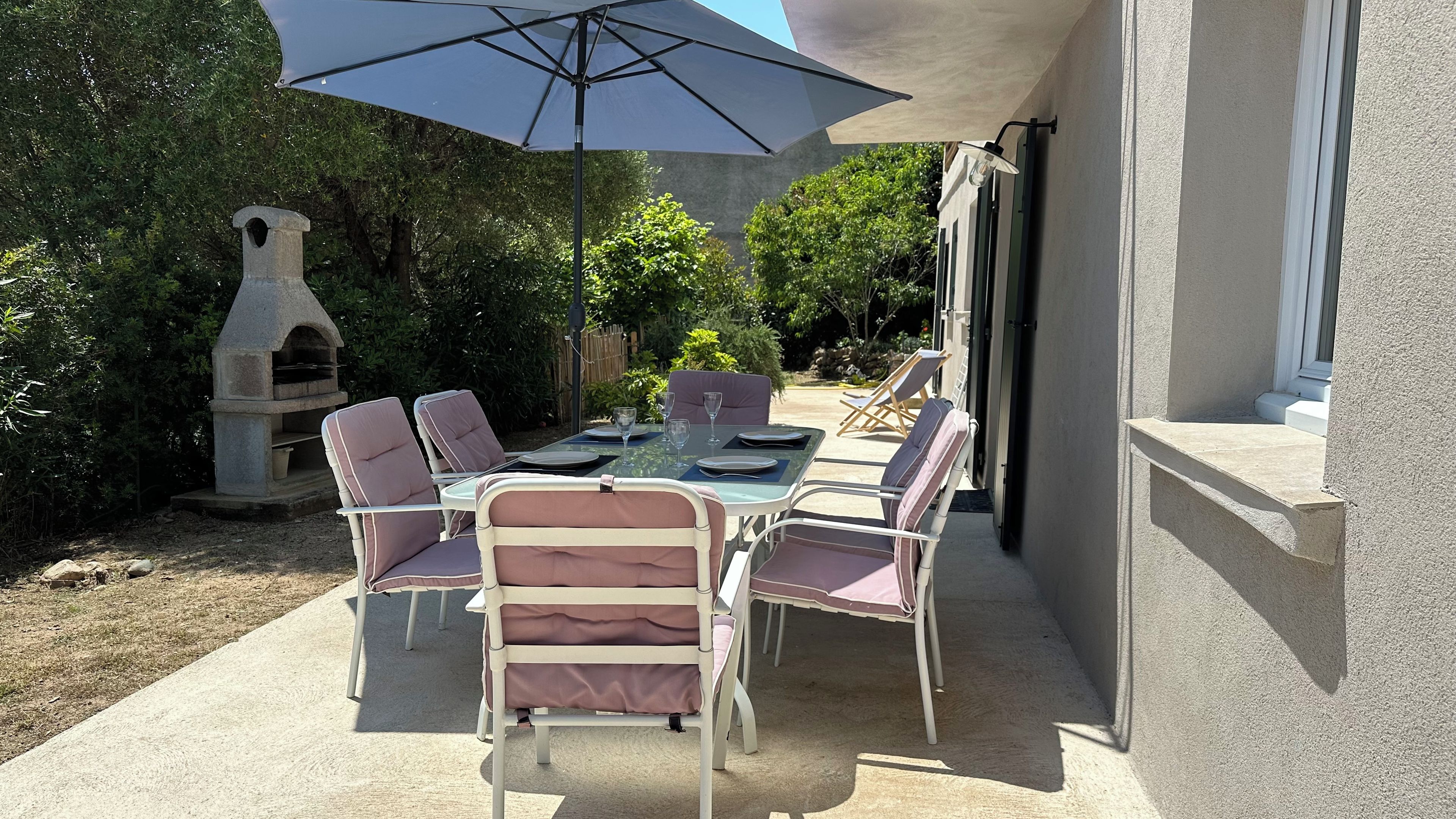 Un patio al aire libre con una mesa para cuatro personas, sillas alrededor y una sombrilla que da sombra.