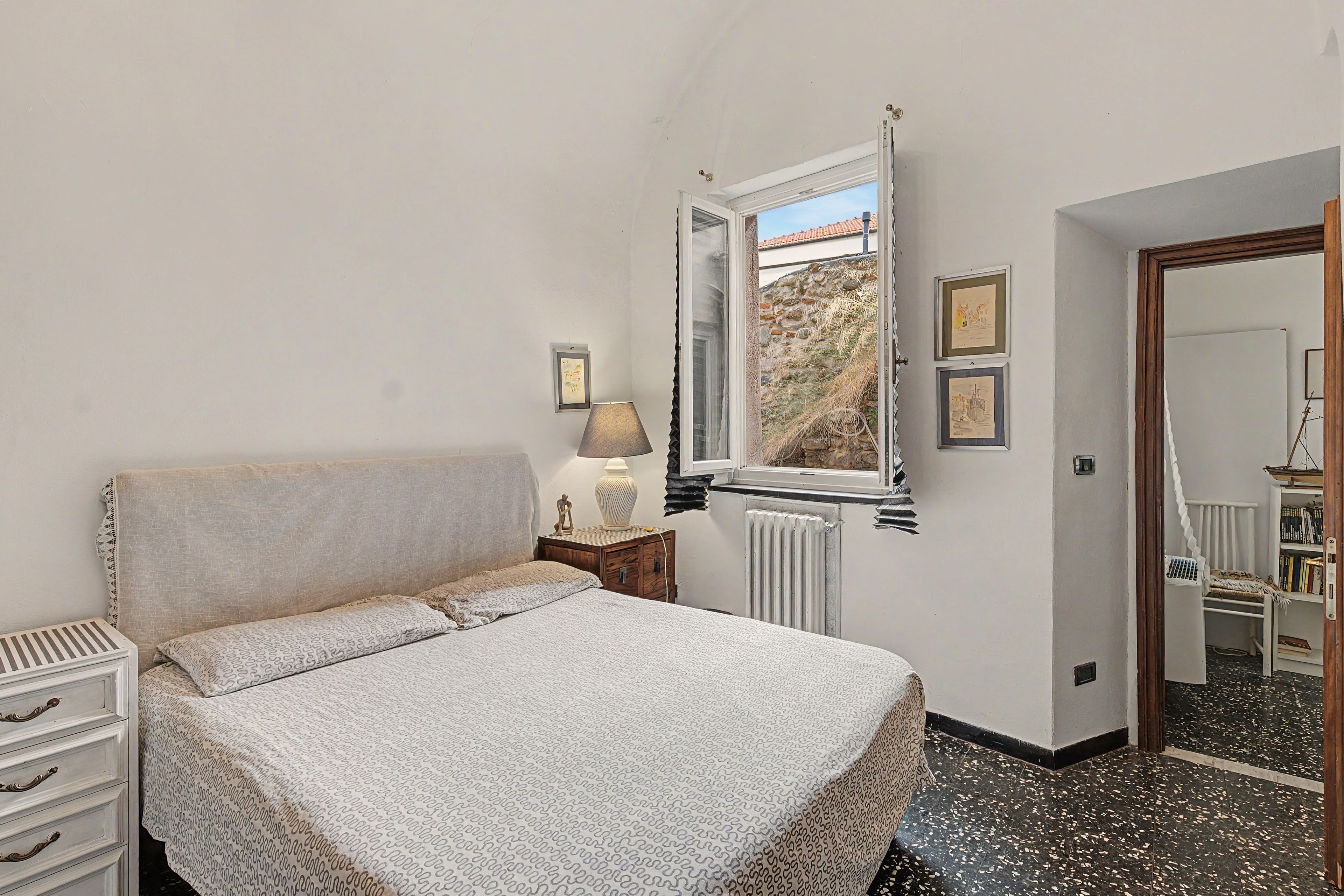 Ein Schlafzimmer mit einem Bett, einem Nachttisch, einer Lampe, einem Fenster und einem Bücherregal.