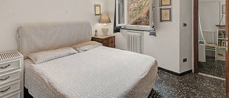 A bedroom with a bed, a nightstand, a lamp, a window, and a bookshelf.