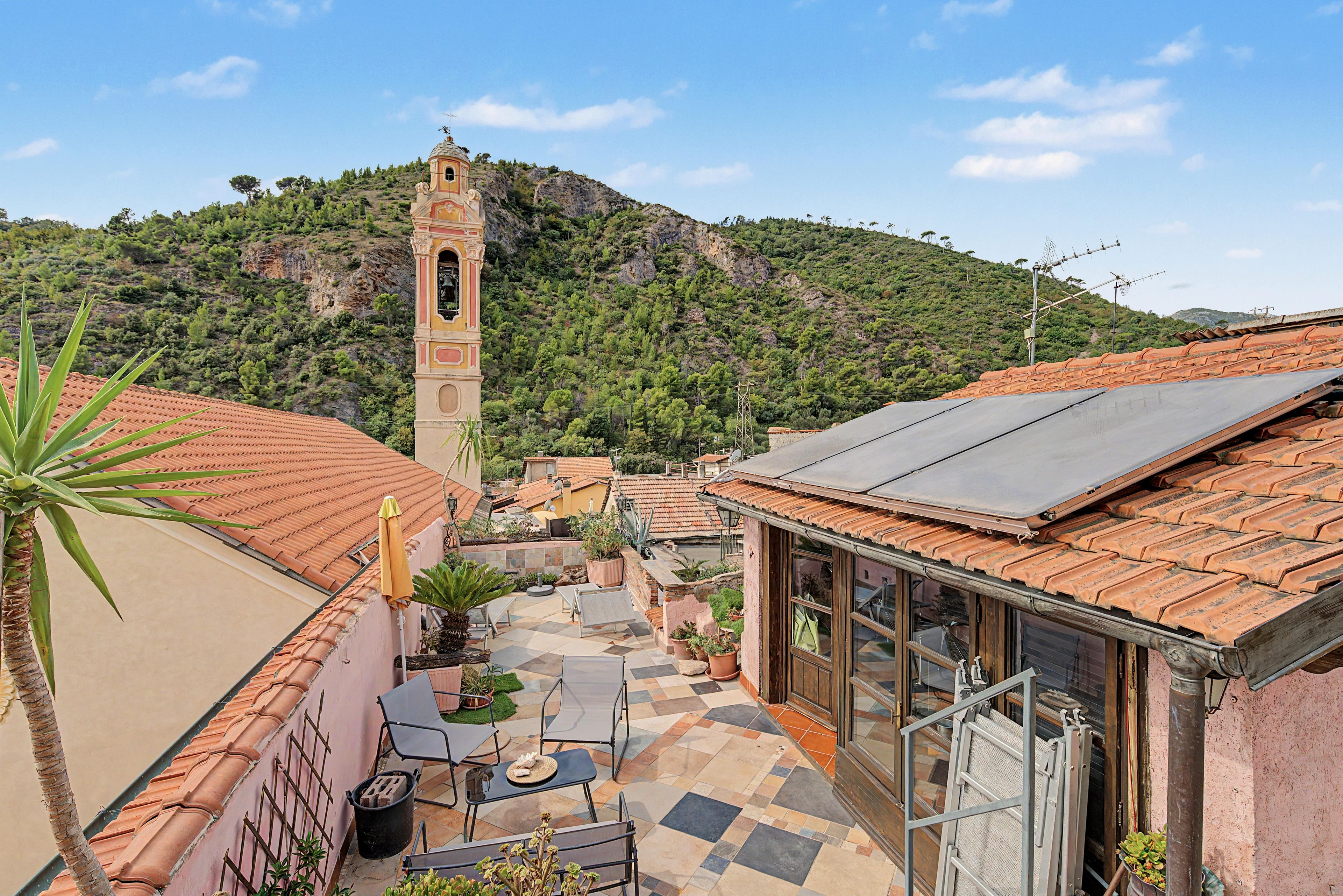 Un pati amb paviment de rajoles, mobles d'exterior i un edifici amb una torre campanar.
