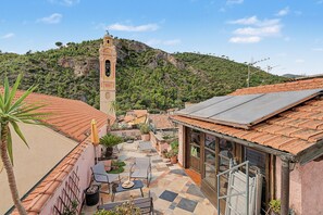 Un pati amb paviment de rajoles, mobles d'exterior i un edifici amb una torre campanar.