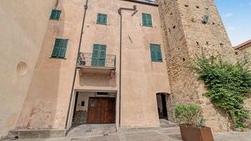 Edifici amb una torre de pedra, una porta de fusta i un balcó amb persianes verdes.