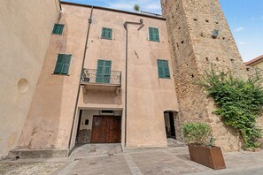 Edifici amb una torre de pedra, una porta de fusta i un balcó amb persianes verdes.