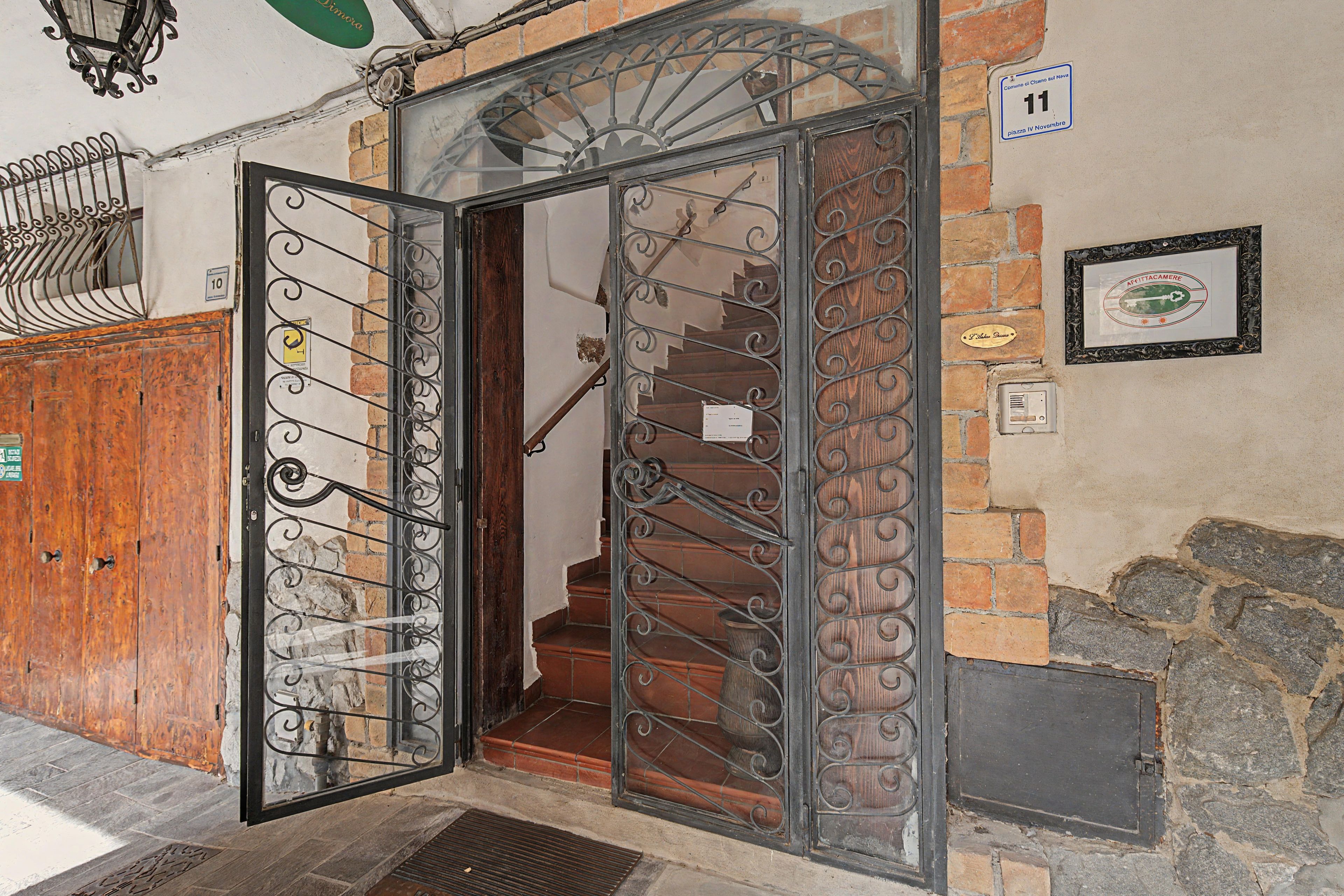 Entrada d'un edifici amb una reixa metàl·lica, una escala i un mur de maó.