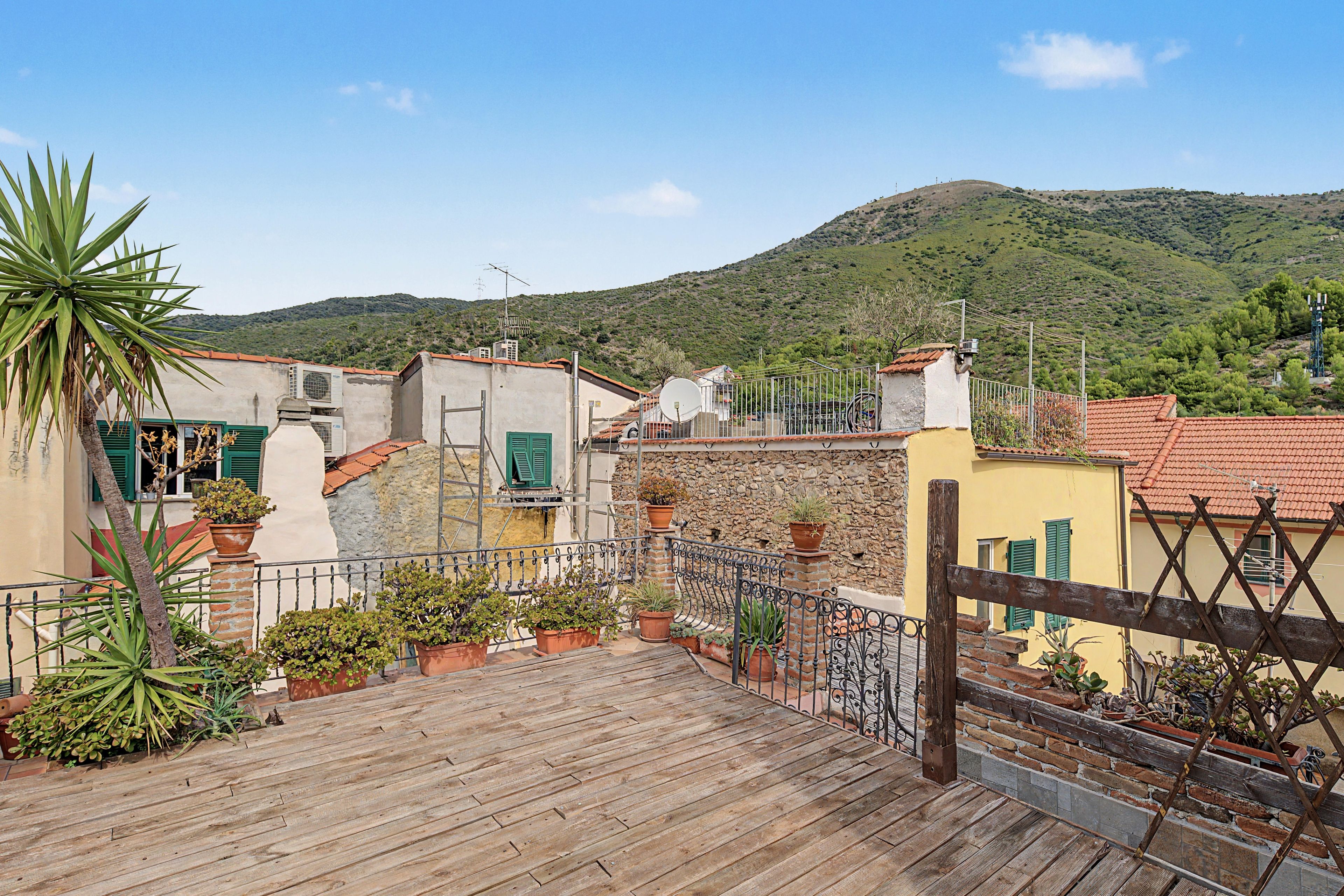 A wooden deck with potted plants, a stone wall, and a view of a hillside.