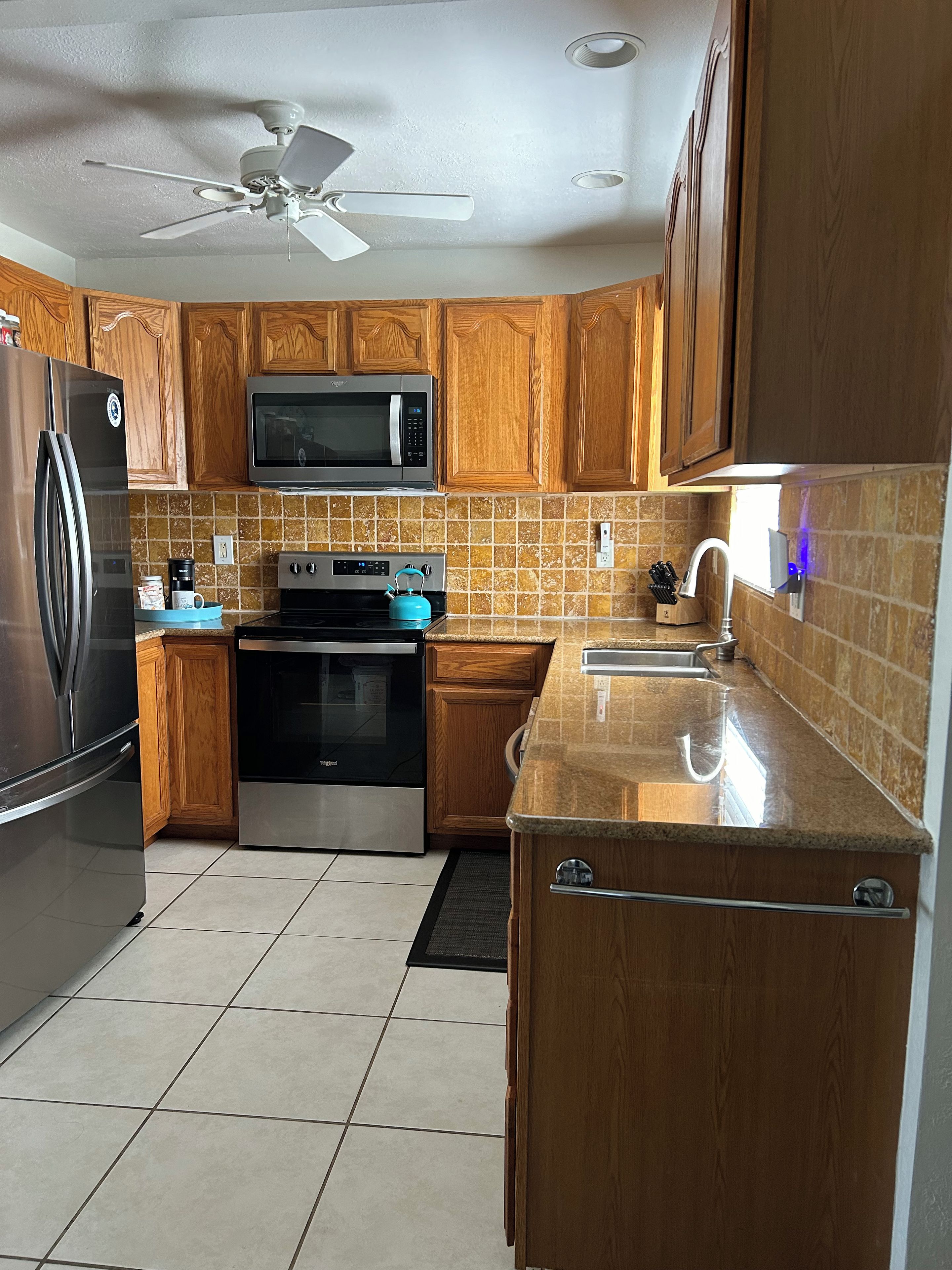 A kitchen with wooden cabinets, a stainless steel refrigerator, a microwave, an oven, and a ceiling fan.