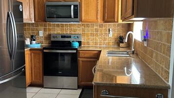 A kitchen with wooden cabinets, a stainless steel refrigerator, a microwave, an oven, and a ceiling fan.