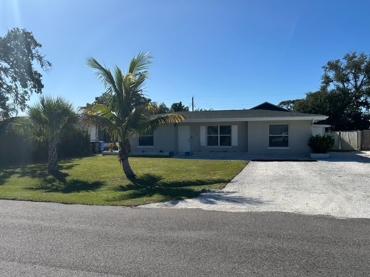 A two-story house with a driveway leading to a garage, surrounded by a lawn and palm trees.