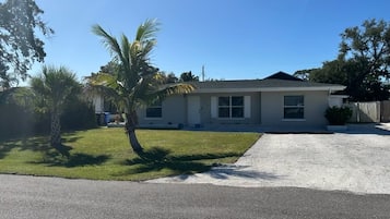 A two-story house with a driveway leading to a garage, surrounded by a lawn and palm trees.