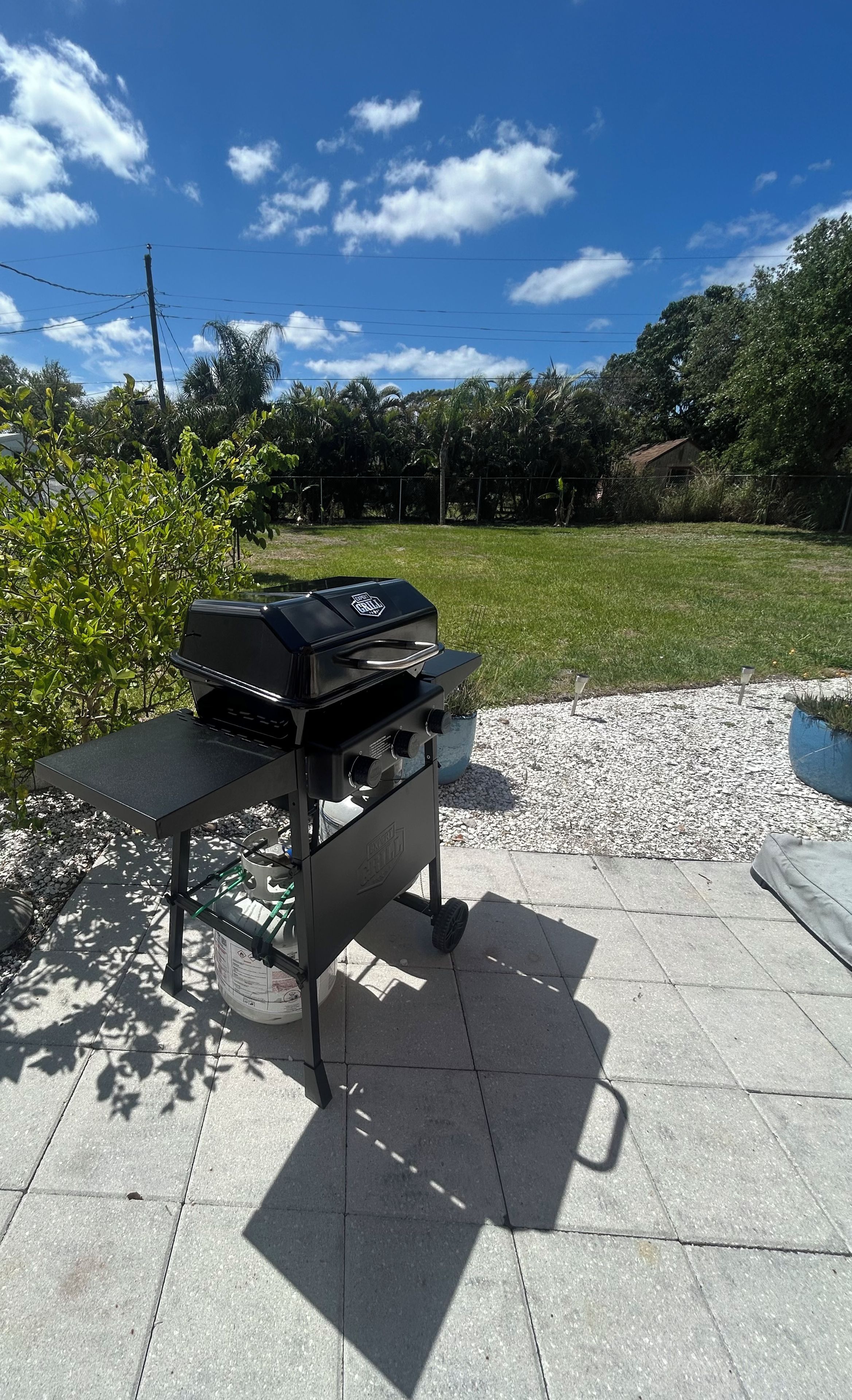 Een buitenbarbecue op een terras, met een heldere lucht en groen in de achtergrond.