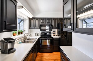 A modern kitchen with dark cabinetry, stainless steel appliances, and a white countertop.