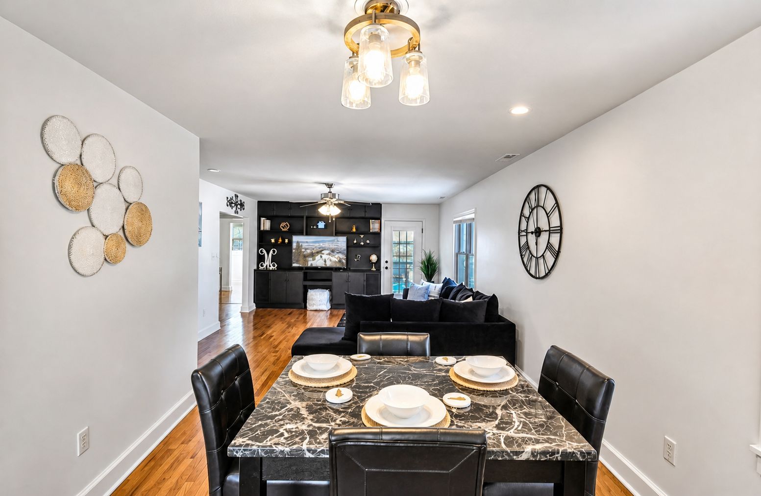 A modern dining room with a marble table set for four, black upholstered chairs, and a black sofa in the background.