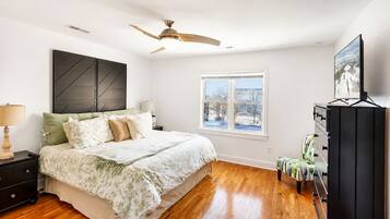A bedroom with a bed, nightstands, a dresser, a ceiling fan, a window with a view, and a dresser with drawers.