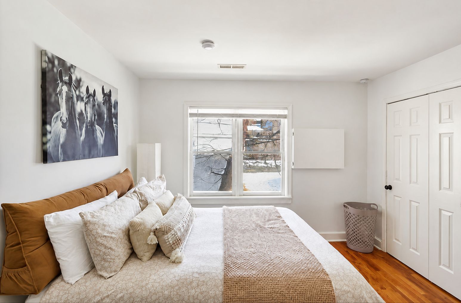 Un dormitorio con cama, ventana, puerta y un cuadro colgado en la pared.