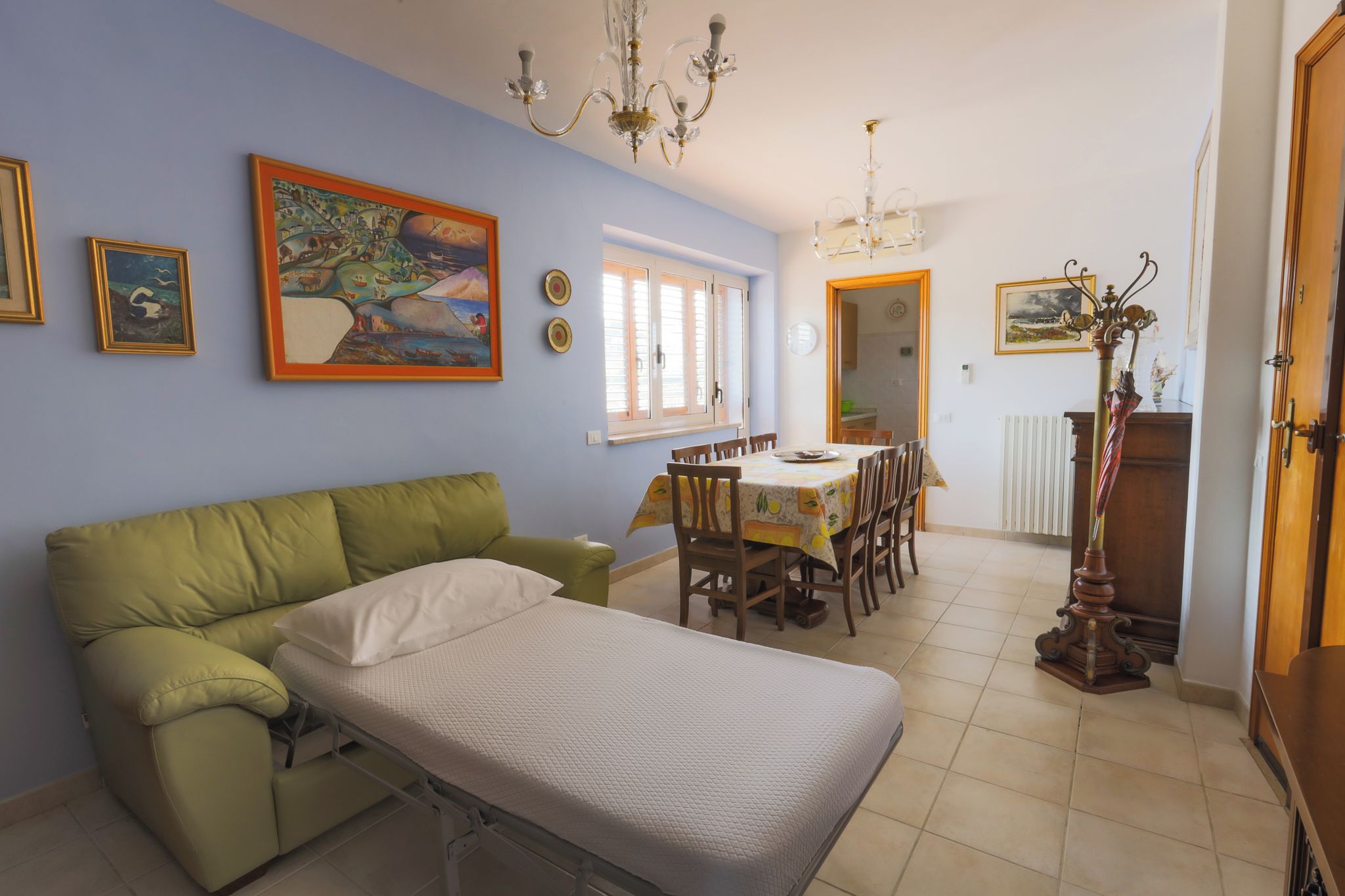 Ein Zimmer mit einem grünen Sofa, einem Esstisch mit Stühlen, einem Bett, einer Kandelaber und einem Gemälde an der Wand.