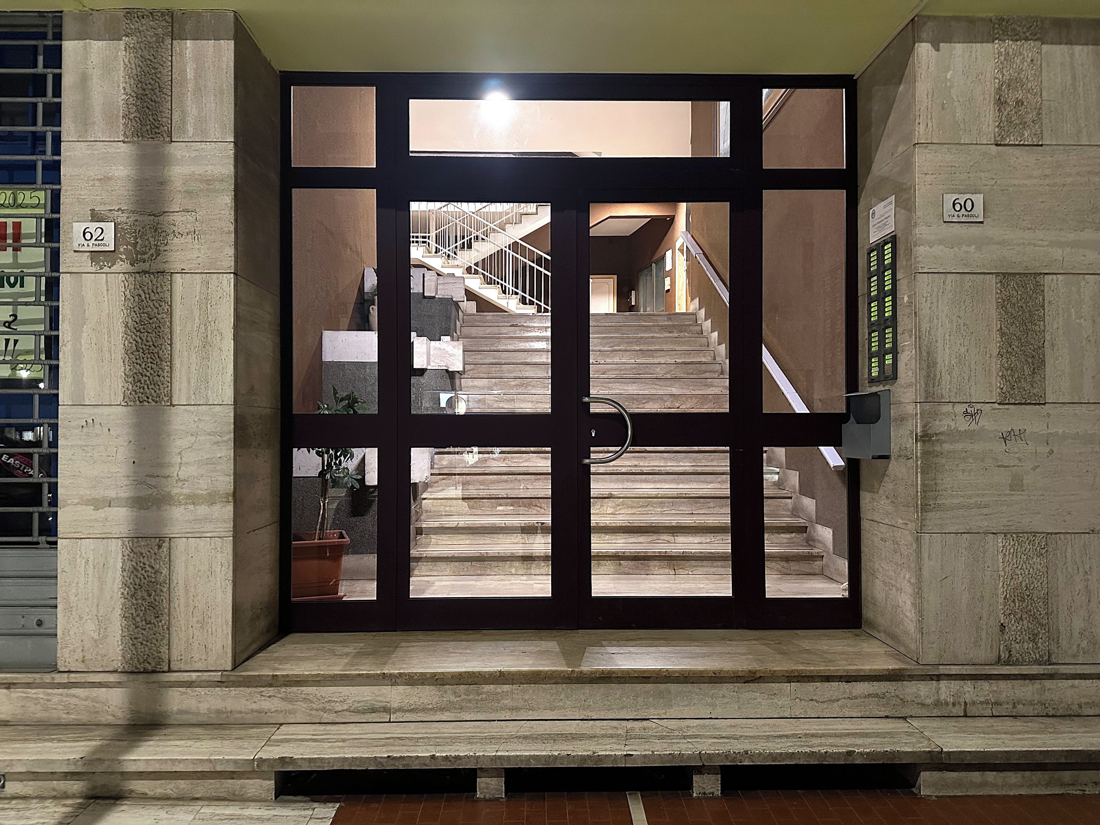 A set of stairs leading to an upper floor, enclosed by a glass door with a metal handle.