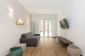 Ein modernes Wohnzimmer mit einem grauen Sofa, einem grünen Hocker, einer Bank und einer Stehlampe.
