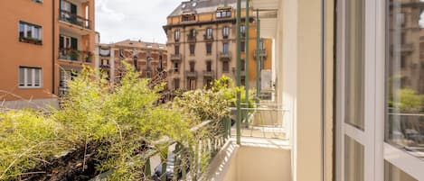 Un balcón con vistas a edificios de varios pisos, una barandilla metálica y cielo despejado.