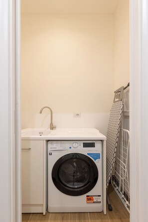 A compact laundry room with a washing machine, a sink, and a drying rack. - Gaffurio Apartment J (Milano)