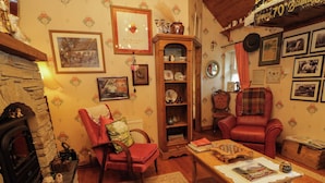 A cozy living room with a fireplace, a red armchair, a wooden table, and a bookshelf. - Teresa's Cottage (Bruckless)