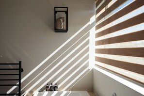 Un baño con bañera, un perchero para toallas y una ventana con persianas.
