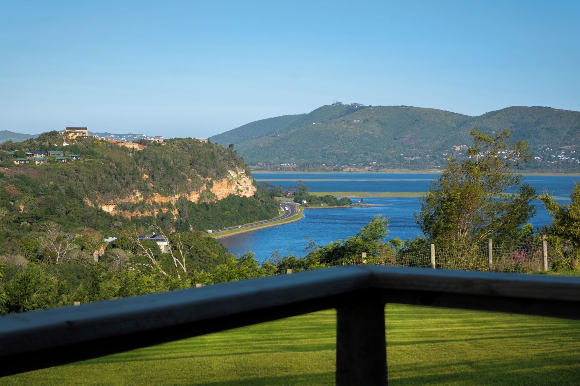 A coastal landscape with a prominent hill, a road curving along the coast, and a body of water.