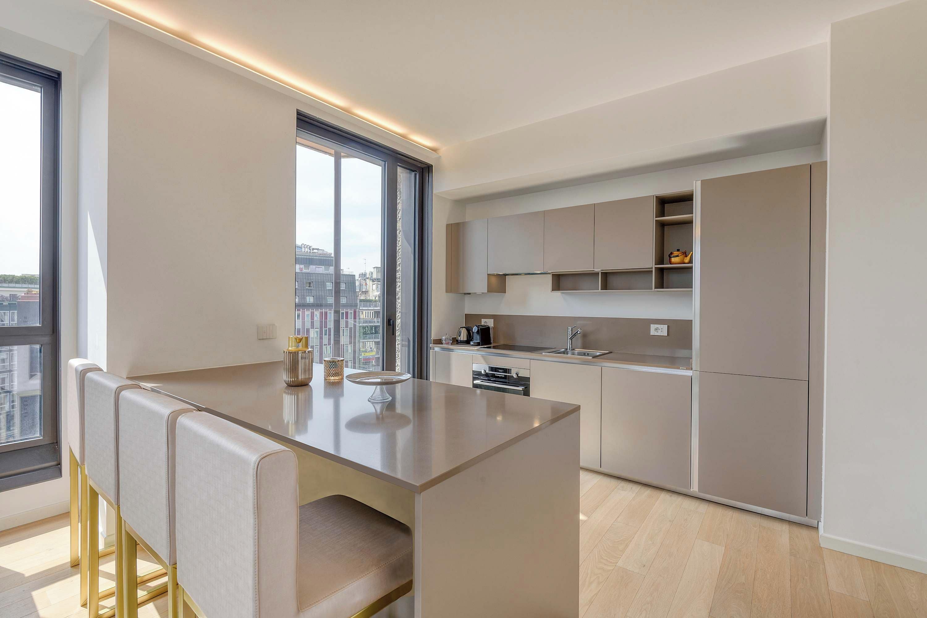 A modern kitchen with a central island, built-in appliances, and a large window offering a city view.