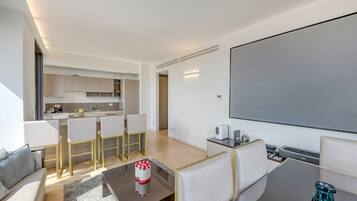 Un soggiorno moderno con una TV a schermo piatto, un tavolino da caffè e un divano. Si intravede in secondo piano una zona cucina con un set tavolo e sedie.