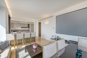 Un soggiorno moderno con una TV a schermo piatto, un tavolino da caffè e un divano. Si intravede in secondo piano una zona cucina con un set tavolo e sedie.