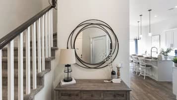 A staircase with a wooden handrail and carpeted steps, a wooden console table with a lamp, a mirror, and decorative items, and a kitchen area with bar stools and a central island.