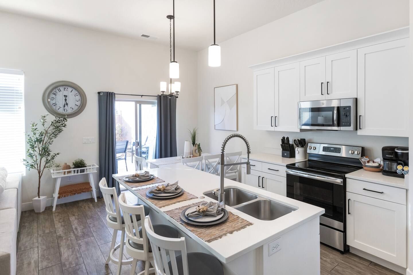 A modern kitchen with white cabinetry, a central island with seating, a stainless steel sink, and a built-in oven.