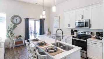 A modern kitchen with white cabinetry, a central island with seating, a stainless steel sink, and a built-in oven.