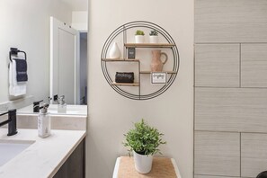 Ein Badezimmer mit Spiegel, Waschbecken, Handtuchhalter und einem Wandregal mit Pflanzen und einem Schild.