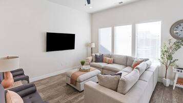 Ein Wohnzimmer mit einem großen Sofa, einem Couchtisch und einem an der Wand befestigten Fernseher.