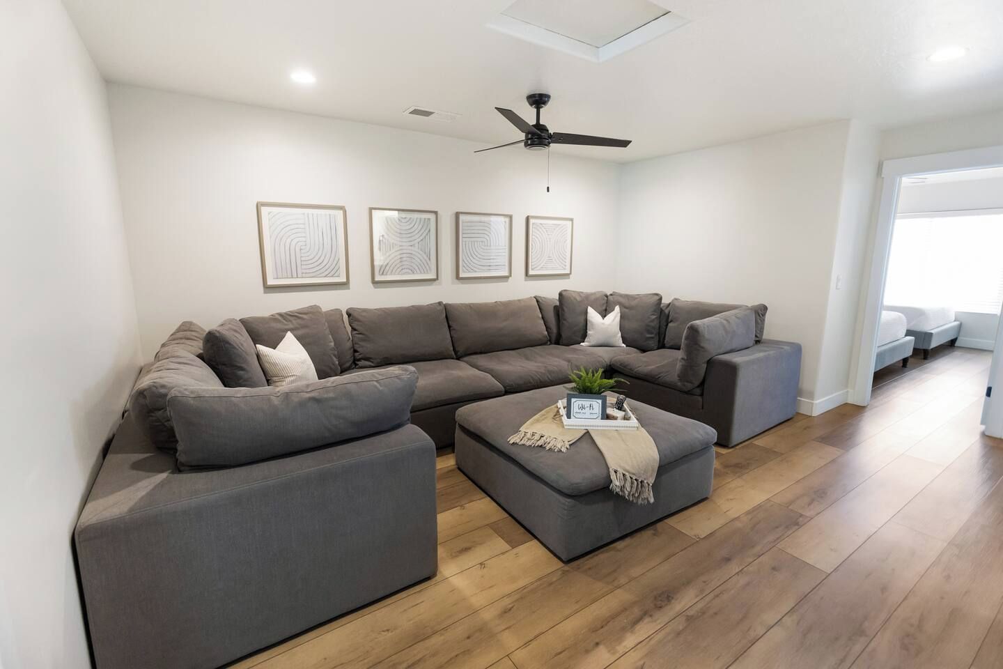 Ein modernes Wohnzimmer mit einem Ecksofa, einem Couchtisch mit Dekoration und einem Deckenventilator.