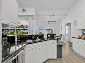 A modern kitchen with white cabinetry, a black countertop, and a view of the outdoors. - Sous le Soleil- Canal, Heated Pool & Beach Gear! (Cape Coral)
