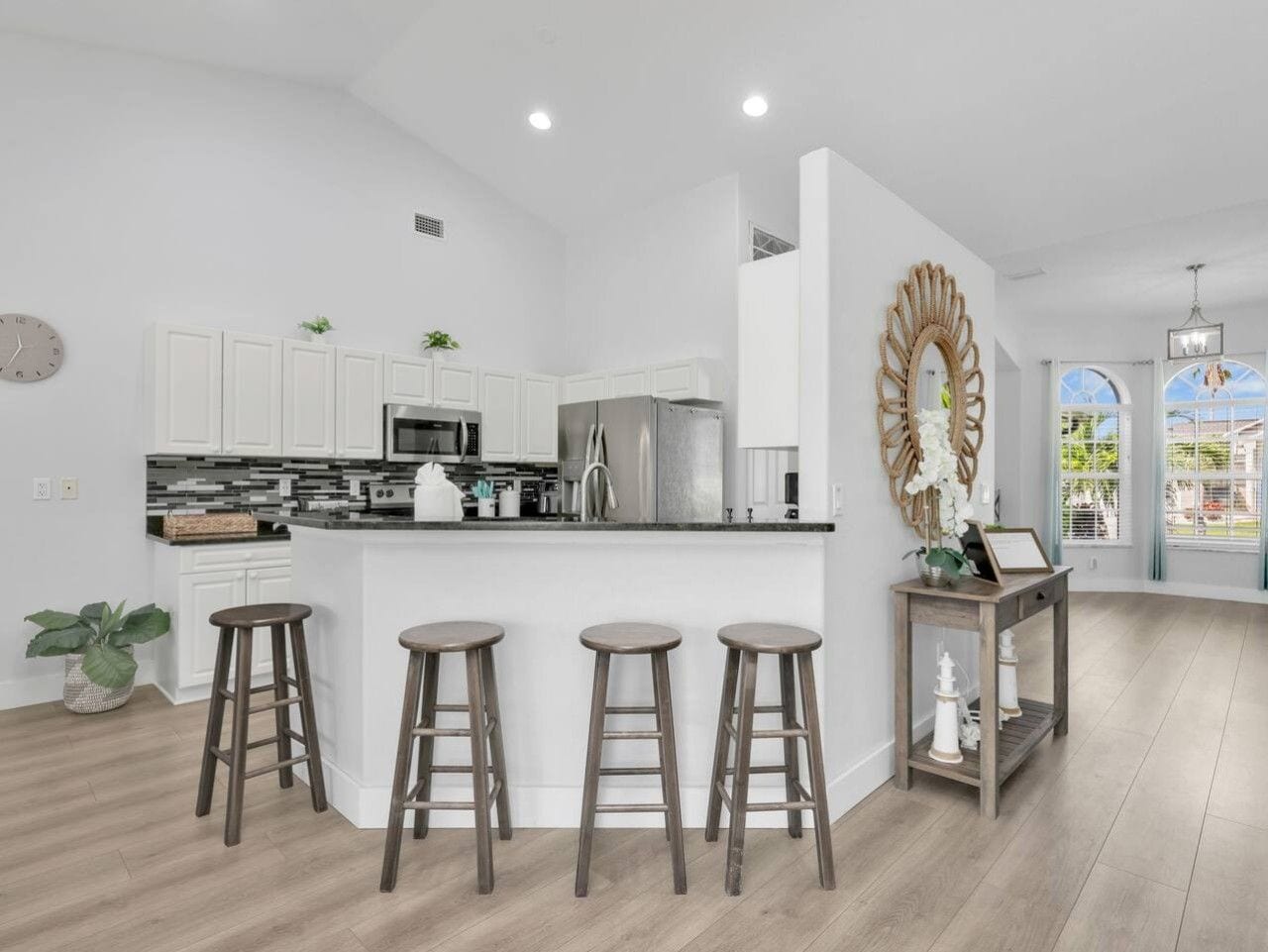 A modern kitchen with white cabinets, a central island with stools, and a decorative mirror.