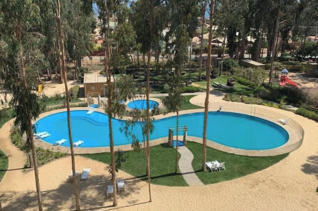 A pool area with multiple swimming pools, surrounded by sand, with pathways and lounge chairs.